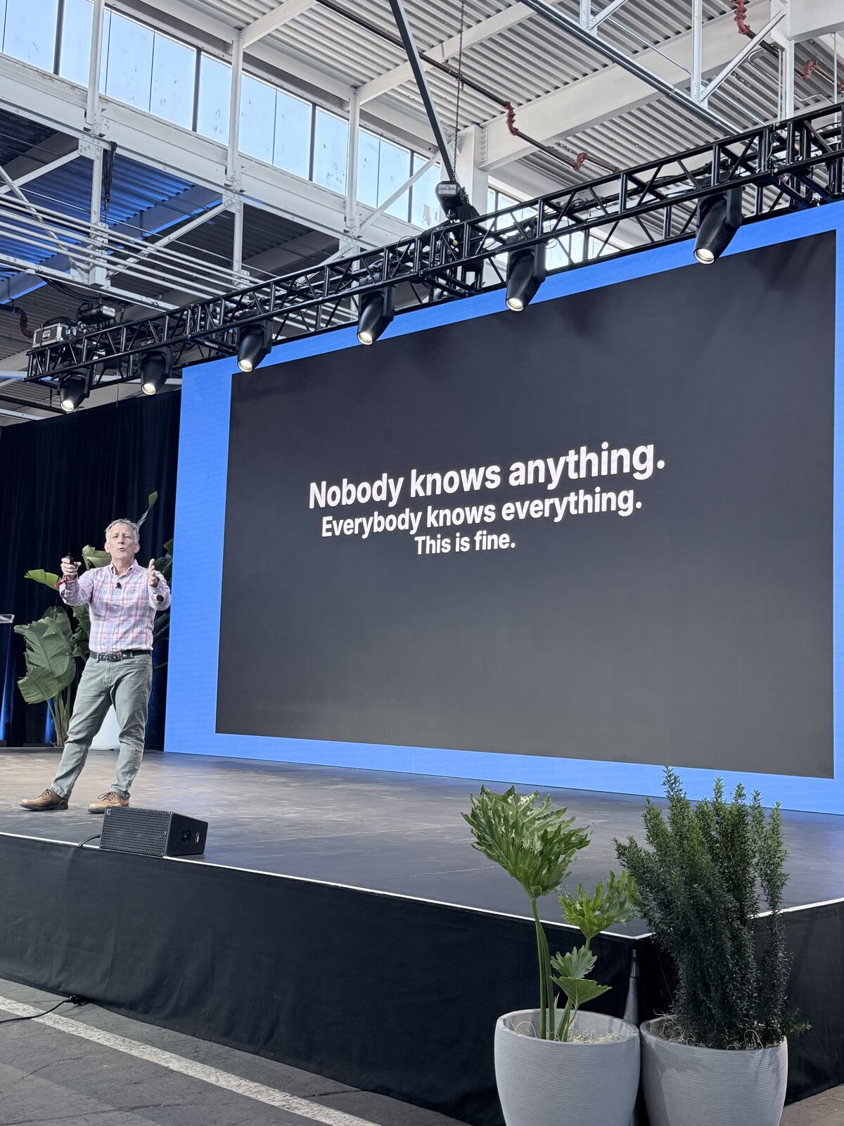 Paul Everitt on stage in front of a slide reading 'Nobody knows anything. Everybody knows everything. This is fine.'