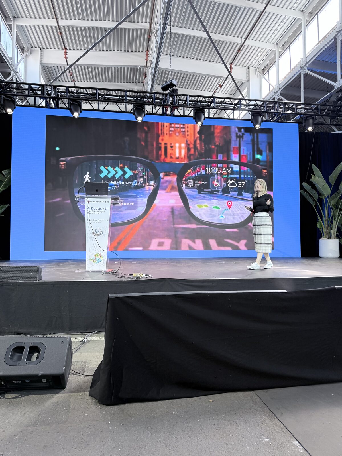 Paige Bailey on stage with a slide showing AR glasses overlaying navigation and weather info on a city street